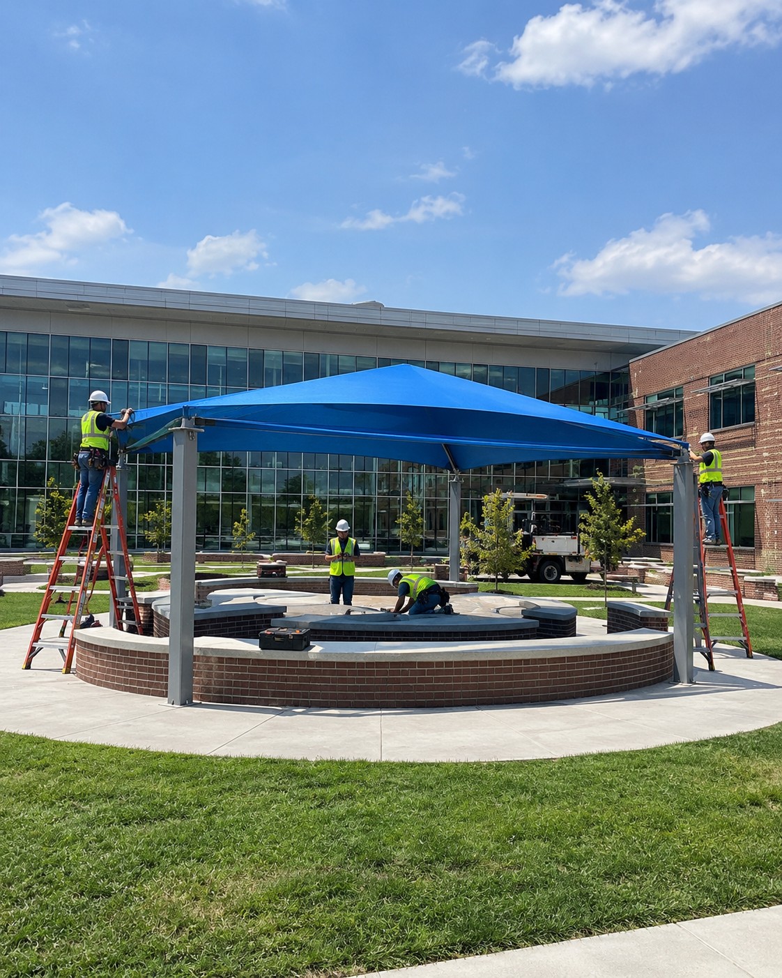 Crew installing a steel-post fabric shade structure over a courtyard seating area